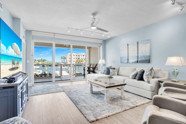 living room with a textured ceiling, light hardwood / wood-style flooring, ceiling fan, and a water view