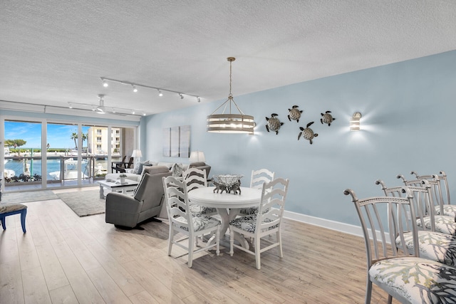 dining space featuring light wood-type flooring, track lighting, a textured ceiling, and a water view