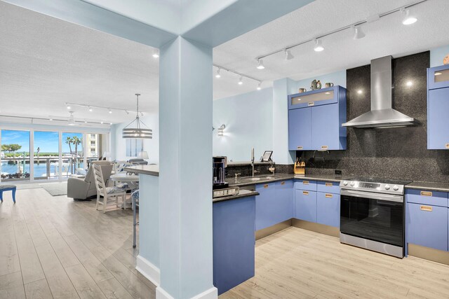 kitchen with blue cabinets, wall chimney range hood, stainless steel electric stove, and a water view