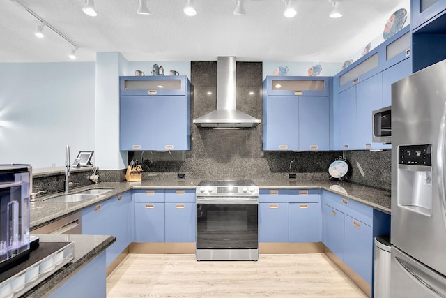 kitchen with appliances with stainless steel finishes, wall chimney exhaust hood, blue cabinets, and sink