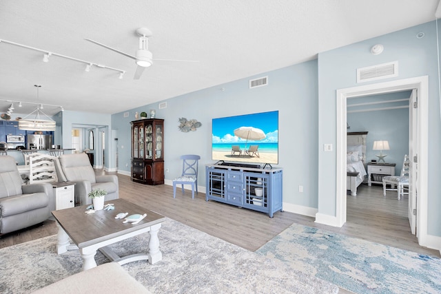 living room featuring ceiling fan, rail lighting, a textured ceiling, and light hardwood / wood-style floors