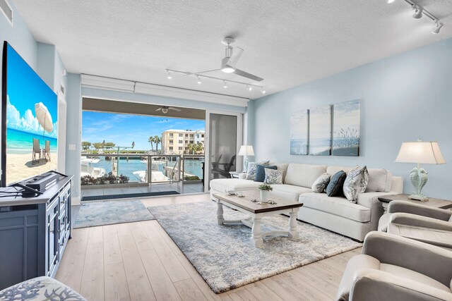 living room featuring a water view, a textured ceiling, ceiling fan, and light hardwood / wood-style flooring