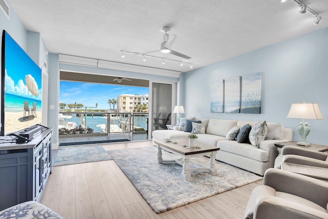 living room featuring a water view, a textured ceiling, ceiling fan, and light hardwood / wood-style flooring