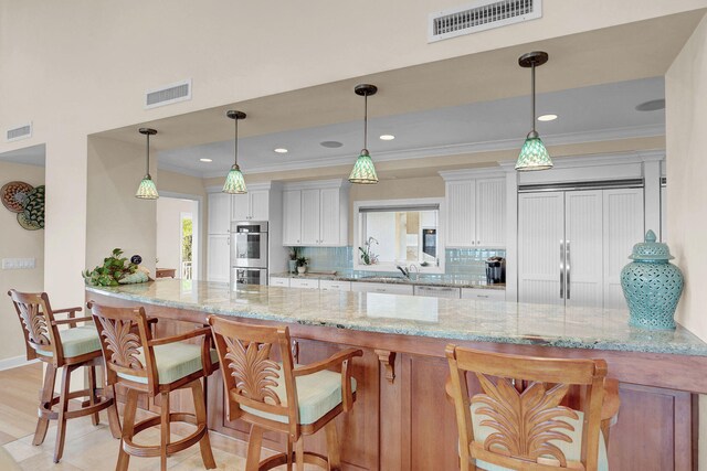 kitchen with light stone counters, pendant lighting, ornamental molding, and white cabinets