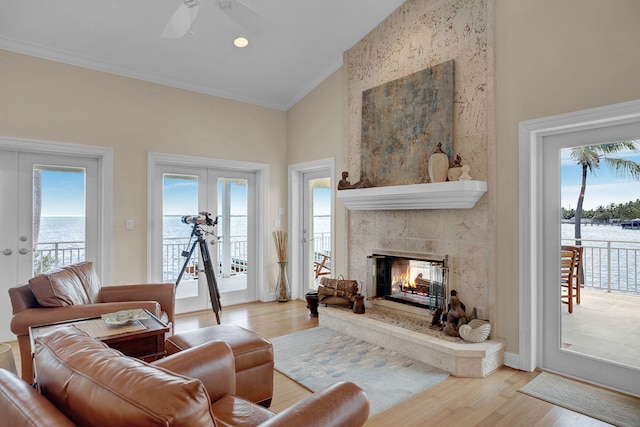 living room featuring french doors, a water view, crown molding, light wood-type flooring, and a tiled fireplace