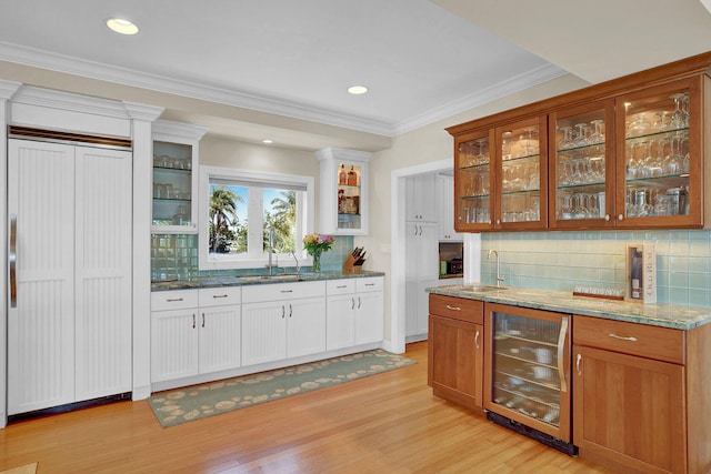 bar with wine cooler, light hardwood / wood-style floors, light stone countertops, and sink