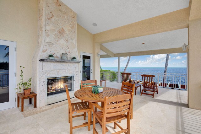 dining room with high vaulted ceiling, a large fireplace, a textured ceiling, and a water view