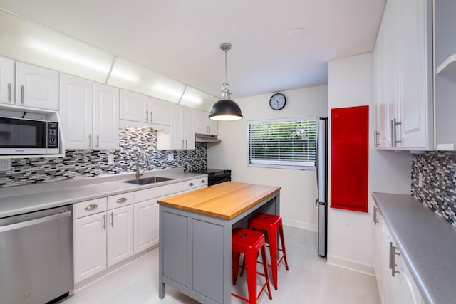 kitchen with decorative backsplash, appliances with stainless steel finishes, hanging light fixtures, white cabinetry, and a sink