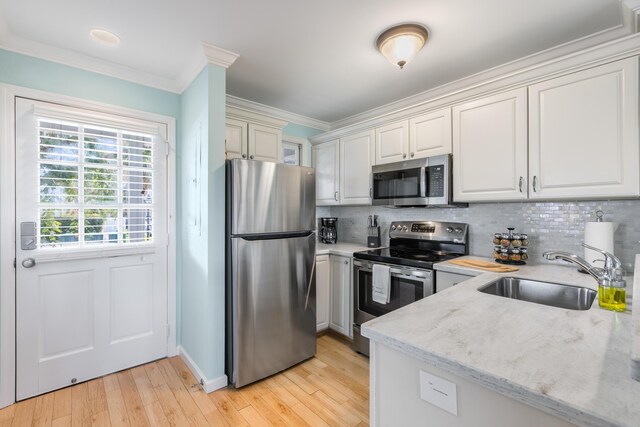 kitchen with sink, stainless steel appliances, light stone counters, ornamental molding, and white cabinets