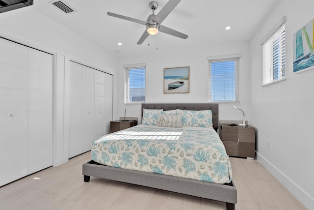 bedroom with two closets, light hardwood / wood-style floors, and ceiling fan