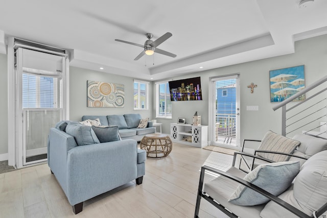 living room with a wealth of natural light, ceiling fan, and a tray ceiling