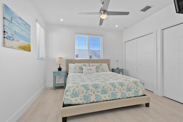 bedroom featuring ceiling fan, light hardwood / wood-style floors, and multiple closets