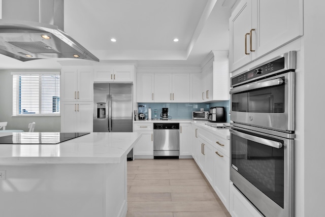 kitchen with appliances with stainless steel finishes, tasteful backsplash, light stone countertops, white cabinets, and island exhaust hood