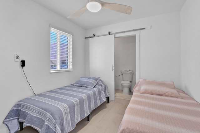 bedroom with connected bathroom, a barn door, ceiling fan, and light wood-type flooring