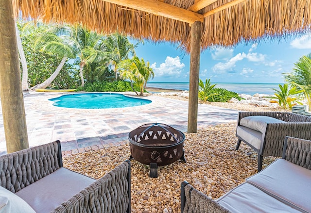 view of swimming pool featuring a fire pit, a gazebo, a patio, a water view, and a beach view