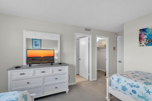 bedroom with light carpet, baseboards, visible vents, a walk in closet, and a textured ceiling