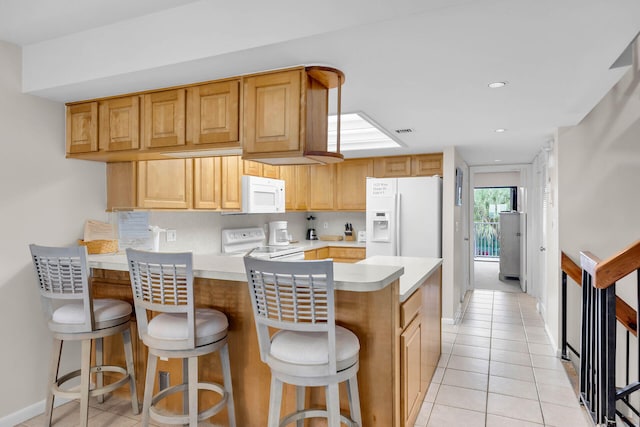 kitchen with light tile patterned floors, light countertops, backsplash, white appliances, and a peninsula