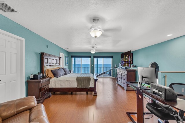 bedroom featuring ceiling fan, hardwood / wood-style floors, access to exterior, and a textured ceiling