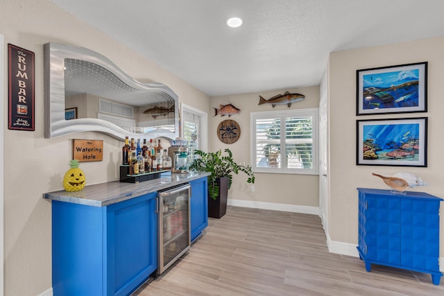 bar with blue cabinets, a textured ceiling, wine cooler, and light wood-type flooring