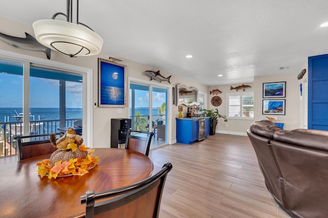 dining space featuring light hardwood / wood-style floors, a textured ceiling, and a water view