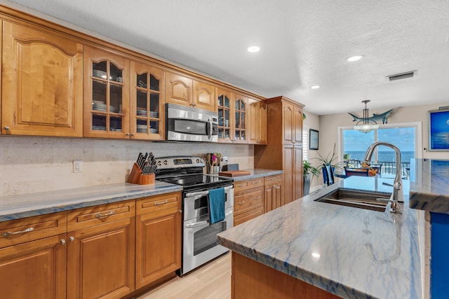 kitchen featuring sink, hanging light fixtures, stainless steel appliances, a textured ceiling, and light hardwood / wood-style flooring