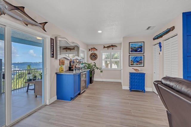 bar featuring wine cooler, blue cabinets, a water view, light stone counters, and light hardwood / wood-style floors