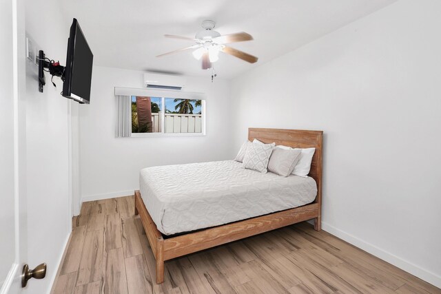 bedroom featuring ceiling fan, light wood-type flooring, and an AC wall unit