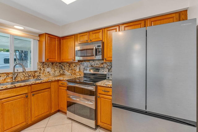 kitchen with light stone counters, appliances with stainless steel finishes, light tile patterned flooring, and sink