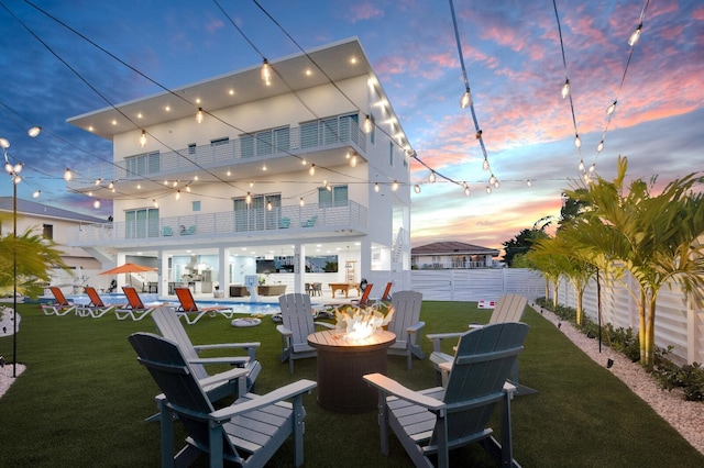 back house at dusk featuring a pool, a fire pit, a lawn, and a balcony