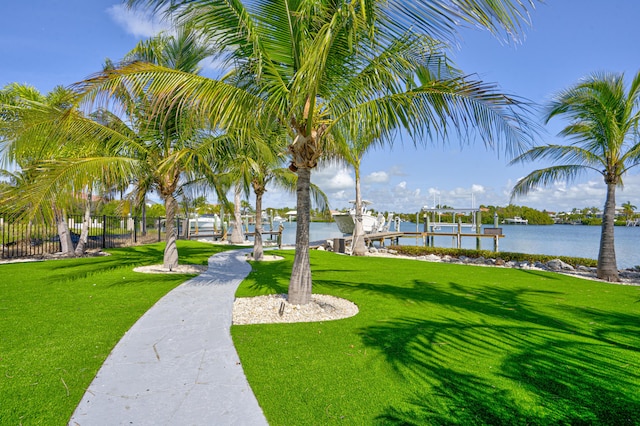 surrounding community featuring a water view, boat lift, fence, and a lawn