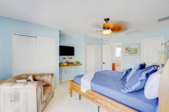 bedroom with a textured ceiling, visible vents, a ceiling fan, multiple closets, and attic access