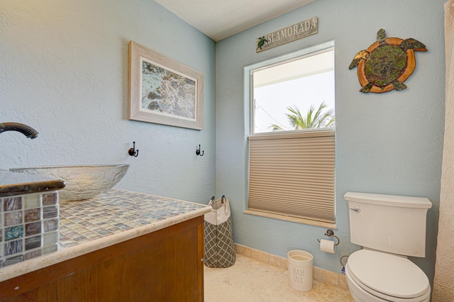 bathroom with baseboards, a textured wall, vanity, and toilet