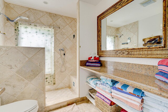 full bathroom featuring toilet, tiled shower, and visible vents