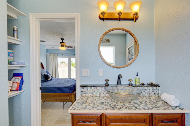 bathroom with a textured wall, a ceiling fan, connected bathroom, vanity, and a textured ceiling