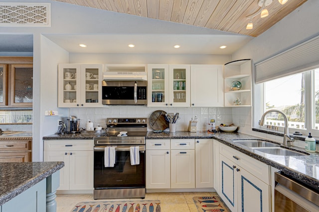 kitchen with stainless steel appliances, dark stone counters, white cabinetry, and a sink