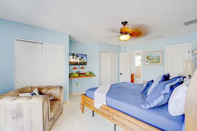 bedroom featuring attic access, visible vents, a ceiling fan, a textured ceiling, and two closets