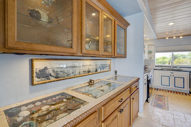 kitchen featuring brown cabinetry, decorative backsplash, glass insert cabinets, light countertops, and a sink