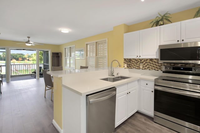 kitchen with appliances with stainless steel finishes, white cabinetry, sink, decorative backsplash, and kitchen peninsula