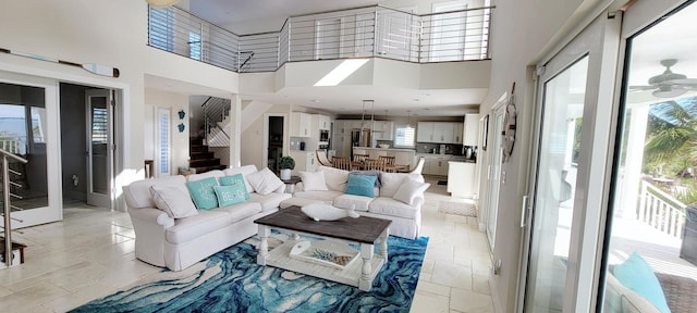 living area featuring stairs, stone tile floors, a towering ceiling, and a ceiling fan