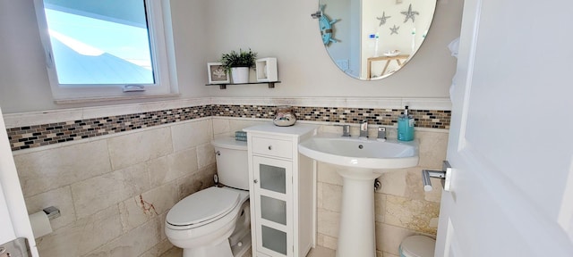 bathroom with toilet, a wainscoted wall, a sink, and tile walls