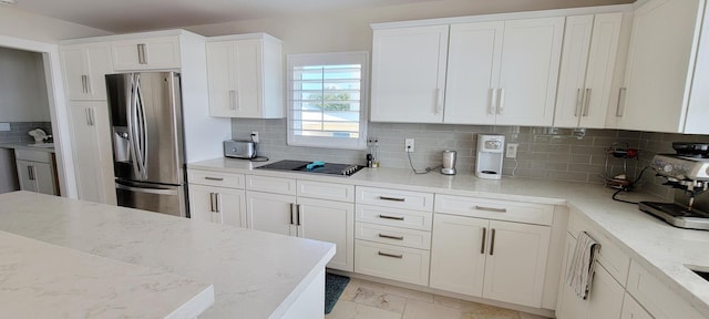 kitchen featuring light stone countertops, stainless steel fridge, black electric cooktop, white cabinets, and decorative backsplash