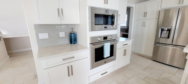kitchen featuring stainless steel appliances, stone tile flooring, tasteful backsplash, white cabinetry, and light stone counters