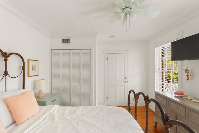 bedroom featuring wood finished floors, visible vents, baseboards, ornamental molding, and a closet