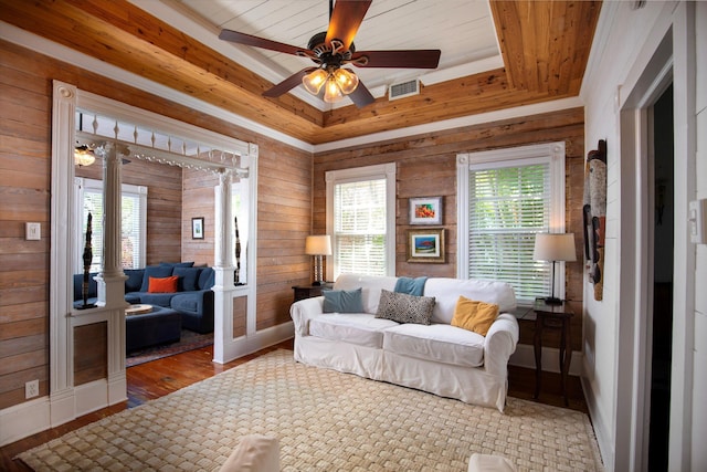 living area with visible vents, a ceiling fan, wood finished floors, a tray ceiling, and wood walls