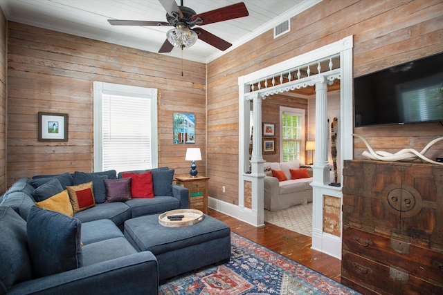 living room with wood walls, wood finished floors, visible vents, decorative columns, and crown molding