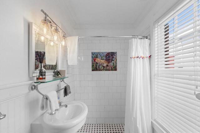 bathroom with crown molding, tile walls, wainscoting, a sink, and tiled shower