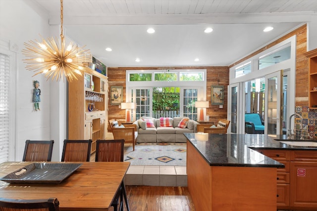 kitchen featuring hardwood / wood-style flooring, wood walls, a sink, beamed ceiling, and an inviting chandelier