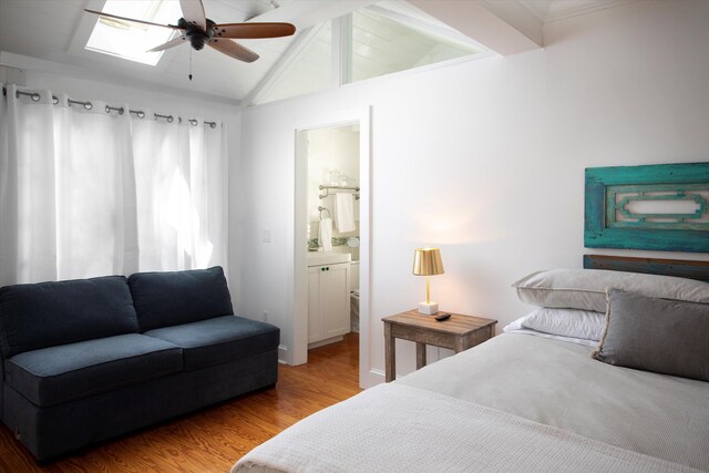 bedroom with a ceiling fan, vaulted ceiling with skylight, ensuite bath, and wood finished floors