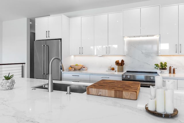 kitchen featuring sink, high end appliances, white cabinetry, light stone counters, and backsplash