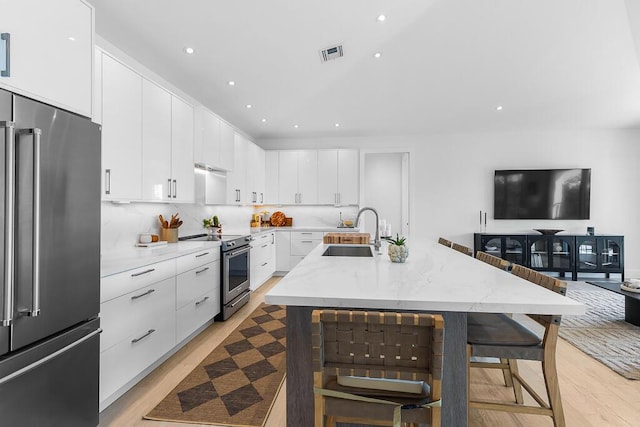 kitchen featuring sink, a breakfast bar area, high end appliances, white cabinetry, and an island with sink